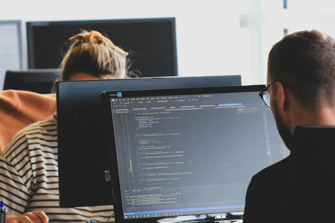 Two developers working at computer monitors, representing persistent AI agents operating across software tools.